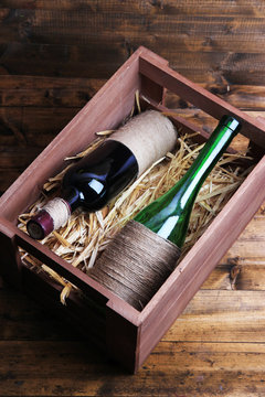 Bottles of wine in wooden box, on wooden background