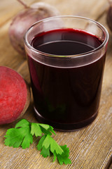 Glass of fresh beet juice and vegetables on wooden background