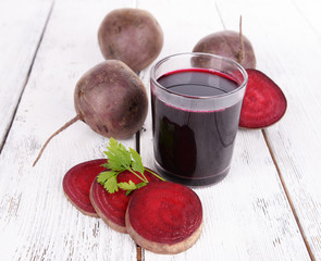 Glass of fresh beet juice and vegetables on wooden background