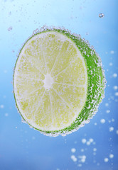 Fototapeta na wymiar Fresh lime in water with bubbles on blue background