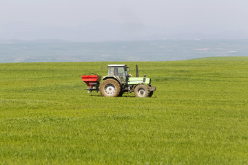 Obraz premium Tractor in green field with mountains in the background over blu