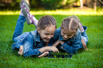 little sisters lying on green grass and playing on tablet