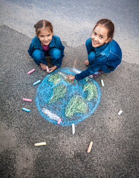 smiling girls drawing Earth with chalks on street