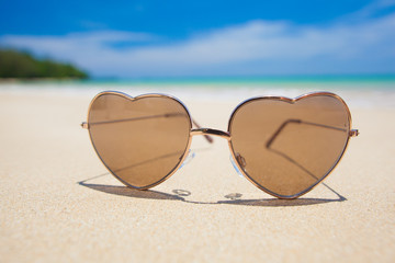 heart shaped sunglasses lying on tropical sand beach. party