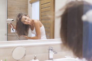 Happy woman drying her hair in bathroom