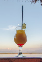 Tequila sunrise cocktail on wooden planks in front of the ocean