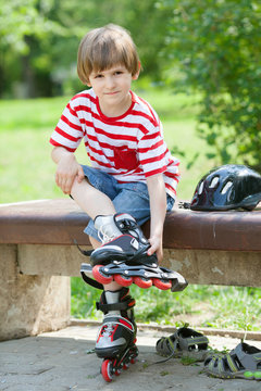 The child put on roller skates on a bench in the summer Park