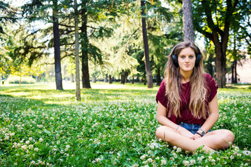 Portrait of young woman listening to music outdoors in a park.