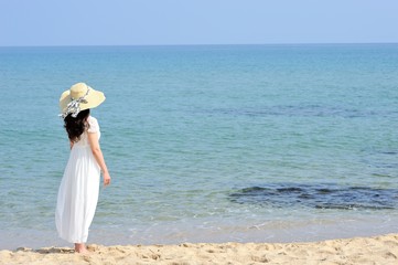Fototapeta na wymiar ビーチで麦わら帽子と白いドレスを着た女性