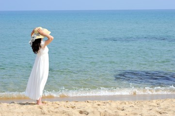 Fototapeta na wymiar ビーチで麦わら帽子と白いドレスを着た女性