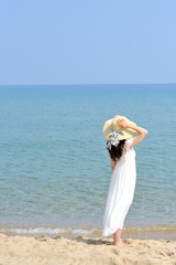 Fototapeta na wymiar 白いワンピースと麦わら帽子を着て海を眺める女性