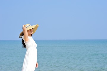 Fototapeta na wymiar 麦わら帽子と白いワンピースを着た女性と夏の海