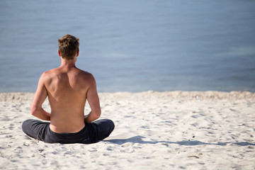 Sitting man doing yoga on shore of ocean