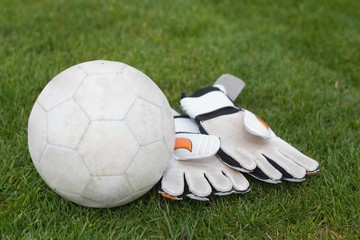 Goalkeeping gloves and football on pitch