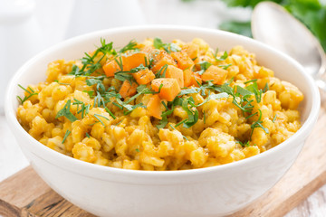 barley porridge with pumpkin and greens in a bowl, close-up