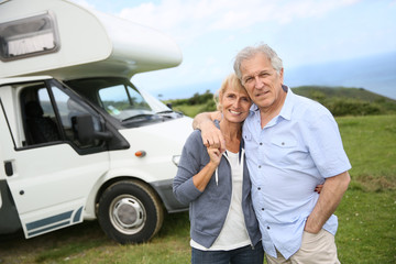 Happy senior couple standing in front of camping car