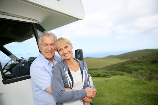 Senior couple standing by motorhome in countryside