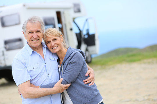 Cheerful senior couple standing by camper on road stop