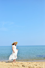 Fototapeta na wymiar 白いワンピースと麦わら帽子を被ったアジア人の美しい女性と夏の海