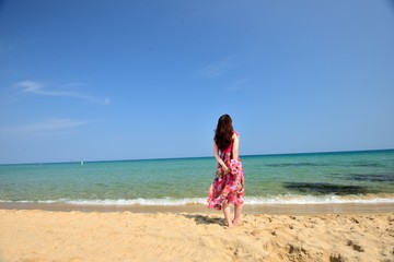 Obraz na płótnie Canvas 海を眺めるピンクのドレスを着た女性の後ろ姿