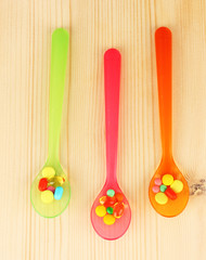 Plastic spoons with color pills on wooden background