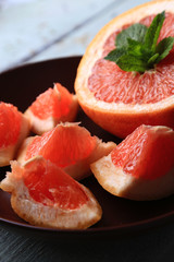 Ripe grapefruits on plate on color wooden background