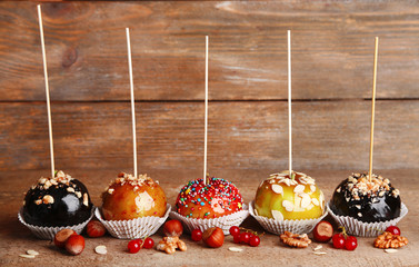 Sweet caramel apples on sticks with berries, on wooden table