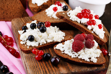 Bread with cottage cheese and berries on wooden board close-up