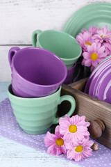 Bright dishes with flowers in crate on wooden background