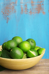 Fresh juicy limes in bowl on blue wooden background