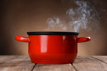 Cooking pot with steam on table on brown background