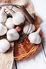 Fresh garlic in basket, on wooden background