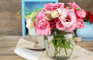 Bouquet of eustoma flowers in vase on wooden background