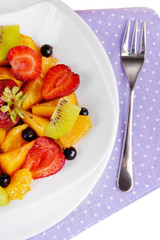 Fresh fruits salad on plate on napkin close up