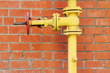Yellow metal gas pipeline with valve on background of red brick