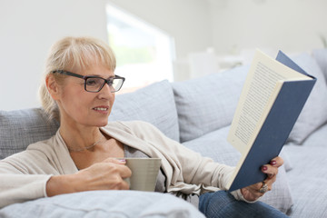 Senior woman reading book and relaxing in sofa