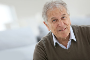 Fototapeta na wymiar Portrait of smiling senior man sitting on sofa at home