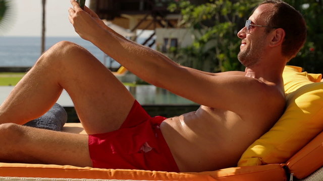 Sunbathing young man on sunbed taking selfie photo 
