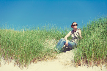 Naklejka na ściany i meble Woman in sand dunes amongst tall grass enjoying sunny day