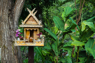 spirit house in thailand with flowers in vases and some wreathes