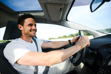 happy handsome young man driving his new car on highway