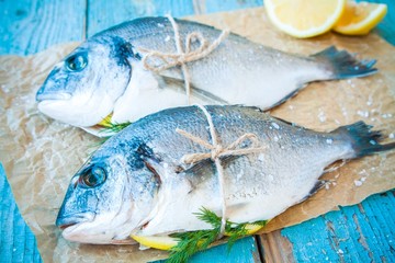 two raw dorada fishes with lemon, green onions and tomatoes