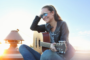 Kobieta w promieniach słońca gra na gitarze akustycznej. - obrazy, fototapety, plakaty
