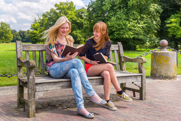 Girls sitting on wooden bench in park reading books