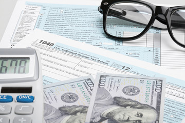 Tax Form 1040 with glasses, calculator and 100 US dollar bills