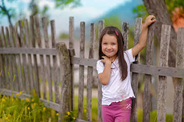 Little girl standing on a background of an old fence