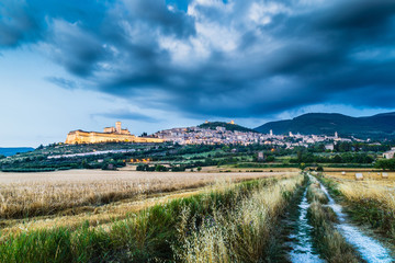 Fototapeta premium Old town of Assisi with dramatic clouds at dusk, Umbria, Italy