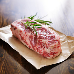 raw new york strip steak on brown parchment paper with rosemary