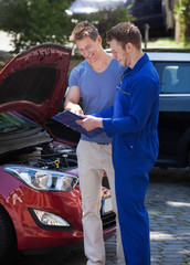 Mechanic Showing Clipboard To Customer By Breakdown Car