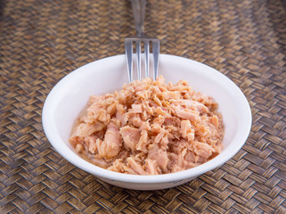 Pieces of canned tuna in a white bowl with a fork on wicker 